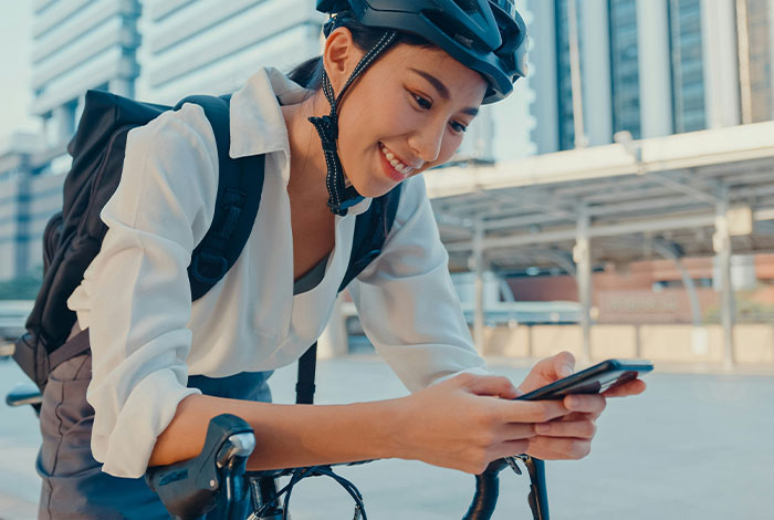 Young woman in bike helmet leaning on bicycle smiling while texting on smartphone outdoors showing social cues misread.
