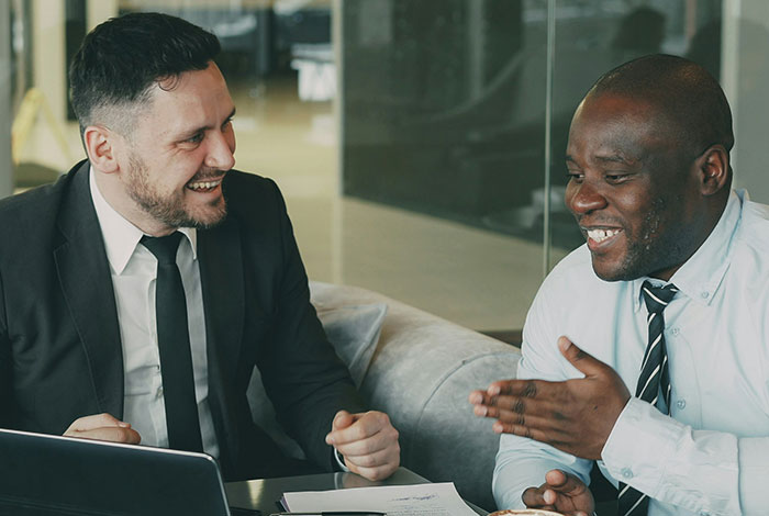 Two men in business attire smiling and talking, illustrating people misreading social cues and creating cringe moments.