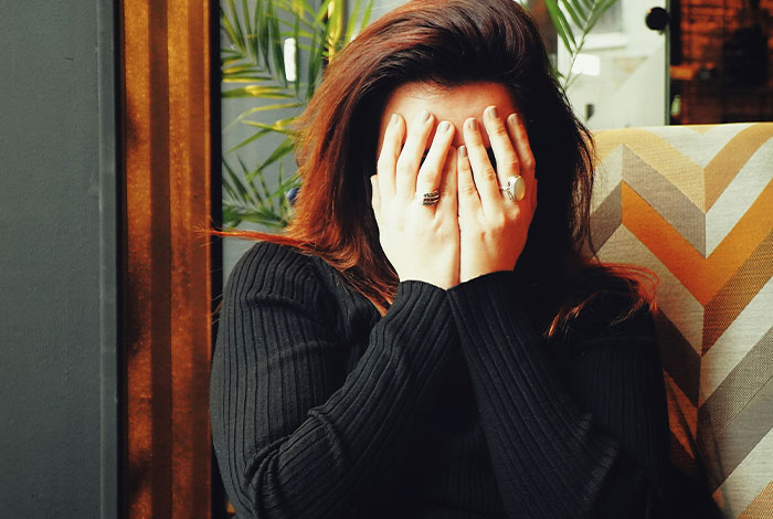 Woman in black sweater covering face with hands, illustrating cringe from misreading social cues in social situations.