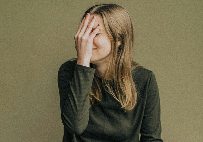 Young woman covering her face in embarrassment, illustrating moments of misread social cues and legendary cringe reactions.