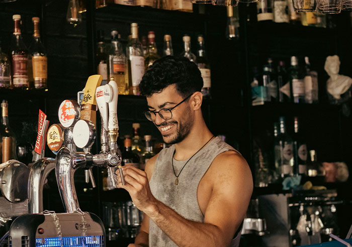 Man with glasses happily pouring a beer at a bar, illustrating social cues and moments of legendary cringe.