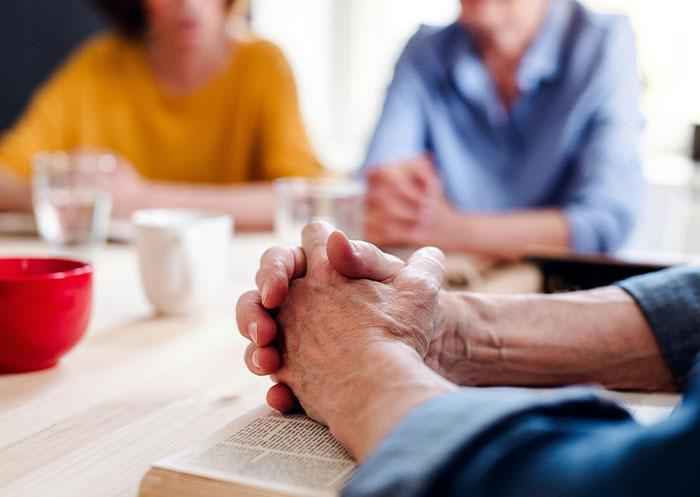 Three people sitting at a table with clasped hands and mugs, illustrating social cues and awkward moments.