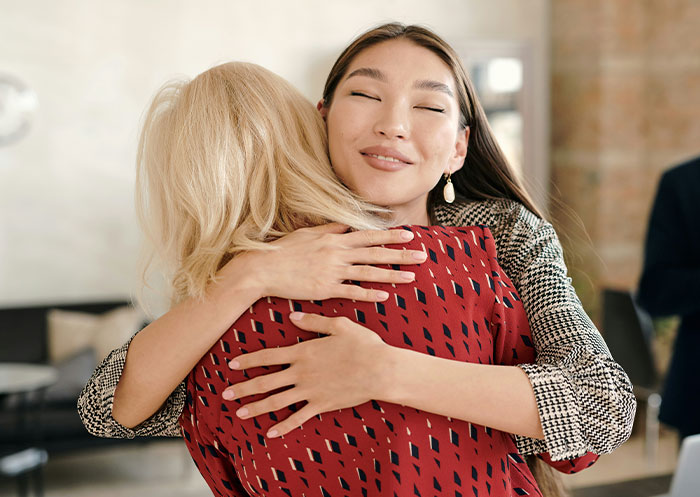 Two women hugging warmly indoors, illustrating social cues and moments of legendary cringe in interactions.