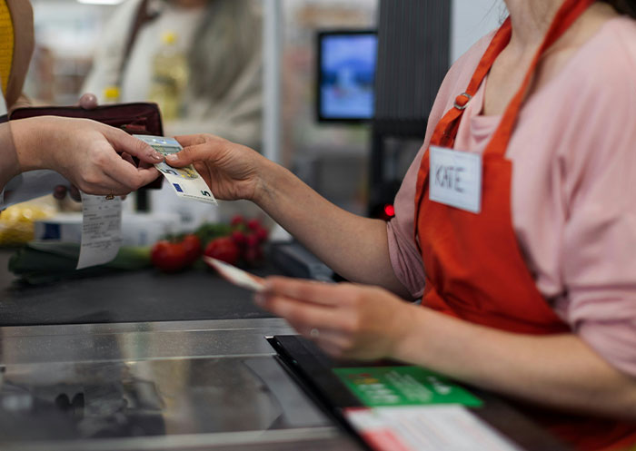 Customer handing money to cashier at grocery store checkout, illustrating social cues and awkward moments.