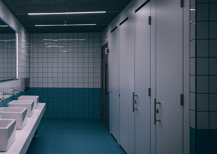 Public restroom with sinks and mirrors on one side, closed white stalls on the other, illustrating social cues misread moments.