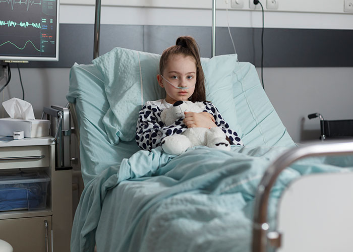 Young girl in hospital bed with oxygen tube, holding a teddy bear, illustrating socially awkward situations story.