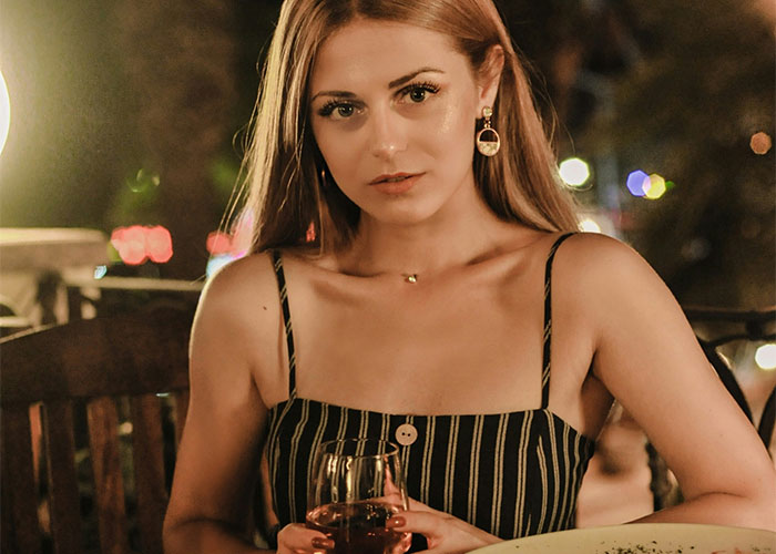 Young woman at a restaurant table looking awkward, holding a glass of drink, illustrating socially awkward situations.