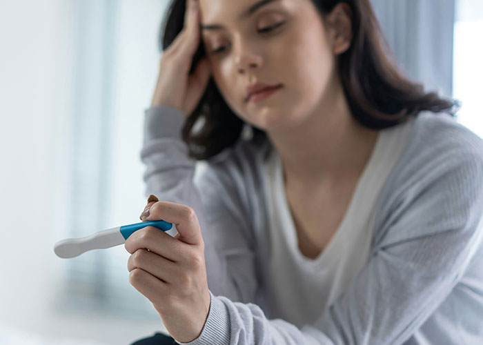 Young woman looking anxious while holding a pregnancy test, illustrating socially awkward situations and emotional moments.