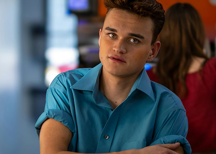 Young man in a blue shirt looking awkward in a social situation with blurred people in the background.