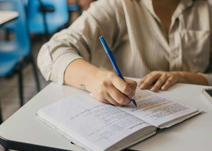 Person writing notes with a blue pen in a notebook, capturing relatable socially awkward situations humorously.