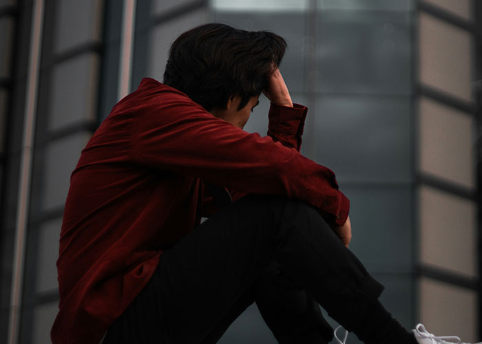 Young man in a red shirt sitting alone, experiencing socially awkward situations in an urban environment.