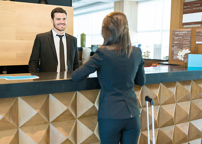 Man in suit smiling at woman with suitcase at hotel reception desk in a socially awkward situation setting.