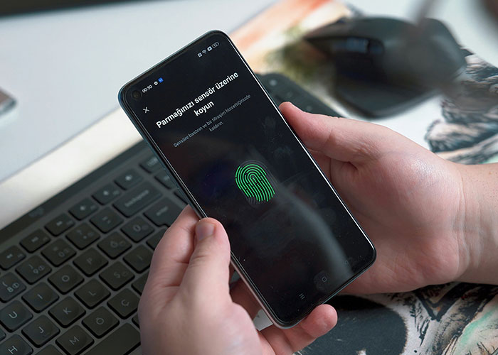 Person holding smartphone with fingerprint scanner active, illustrating socially awkward situations with technology usage.