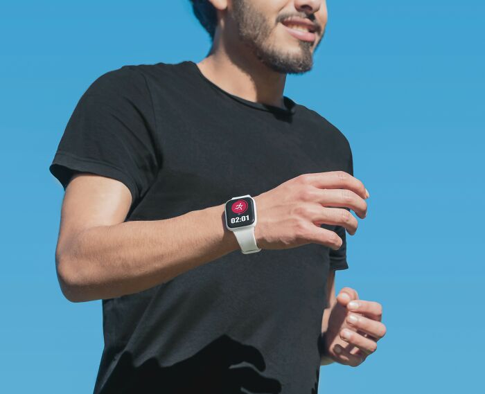 Man wearing a black shirt and a smartwatch running outdoors under a clear blue sky focused on tracking activity.