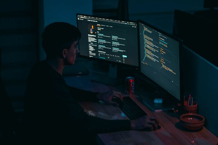Person working at dual computer screens late at night, illustrating people who lost jobs to AI in tech-related roles.