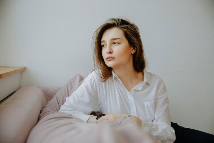 Young woman in white shirt sitting on couch looking away, reflecting frustration with deadbeat dad and free sitting duties. Young woman in white shirt sitting on couch looking away, reflecting frustration with deadbeat dad and free sitting duties.