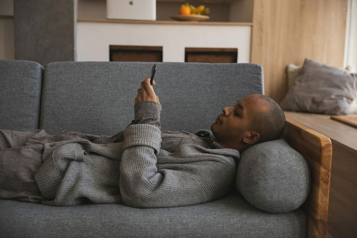 Man lying on sofa using phone, illustrating deadbeat dad ignoring responsibilities and leaving kids to GF's daughter. Man lying on sofa using phone, illustrating deadbeat dad ignoring responsibilities and leaving kids to GF's daughter.