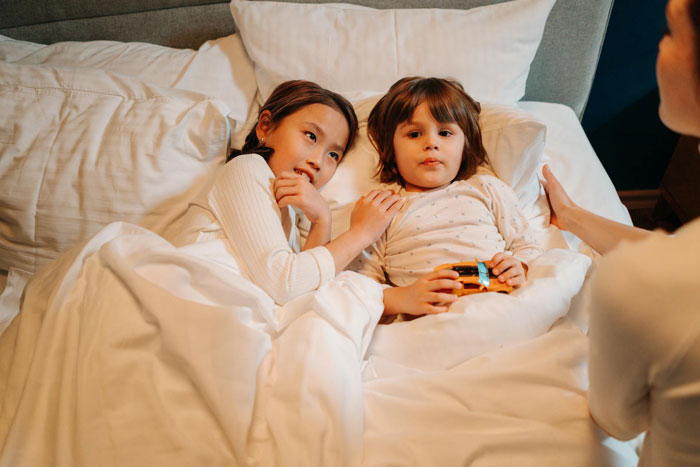 Two young children lying in bed with a woman nearby, illustrating deadbeat dad dumping kids on girlfriend’s daughter. Two young children lying in bed with a woman nearby, illustrating deadbeat dad dumping kids on girlfriend’s daughter.