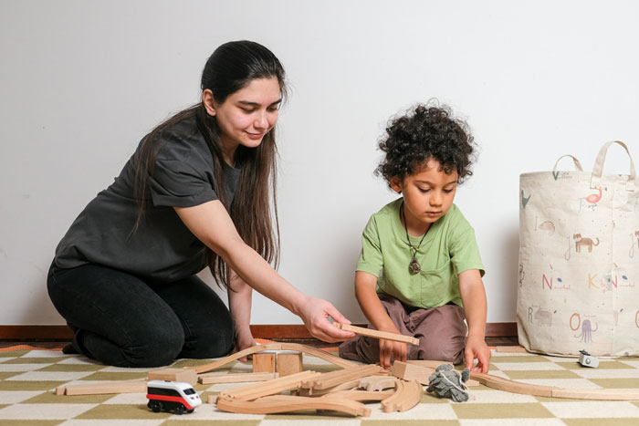 Woman and child playing with wooden train set indoors, illustrating deadbeat dad dumping kids on girlfriend's daughter scenario. Woman and child playing with wooden train set indoors, illustrating deadbeat dad dumping kids on girlfriend's daughter scenario.