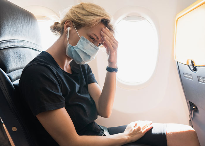 Passenger wearing a face mask on an airplane, looking stressed after an 8-hour toddler meltdown during the flight.