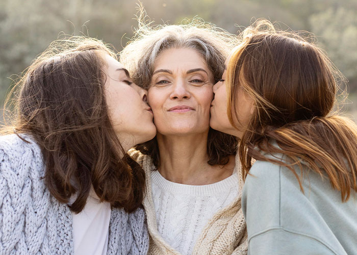 Mom with two daughters outdoors, showing affection with kisses, highlighting mom admits she likes one daughter more than the other.