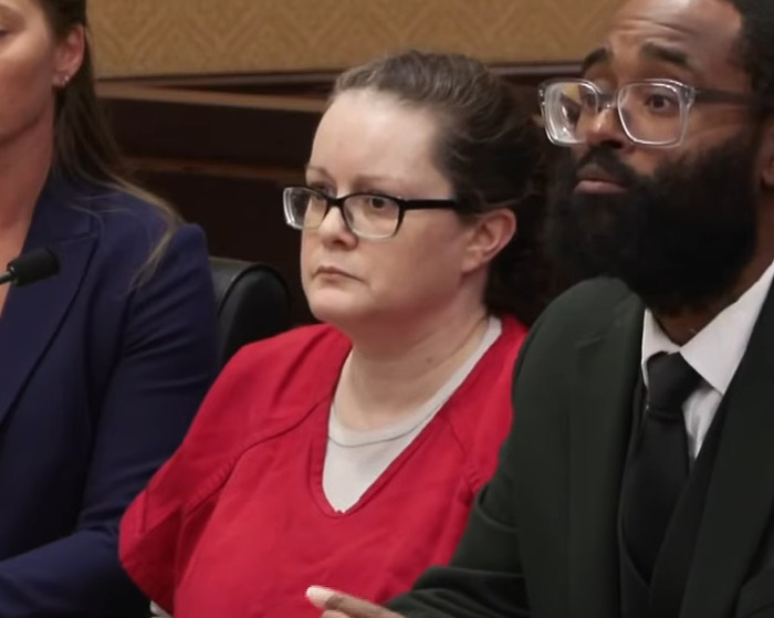 Woman in red prison uniform with glasses sitting in court during a hearing about a haunting 911 call case.