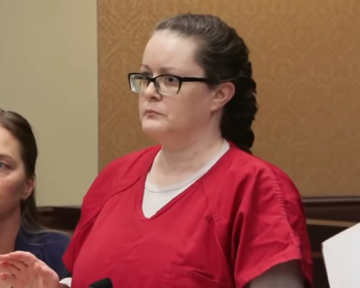 Woman in red prison uniform standing in courtroom during a case related to haunting 911 call confession.