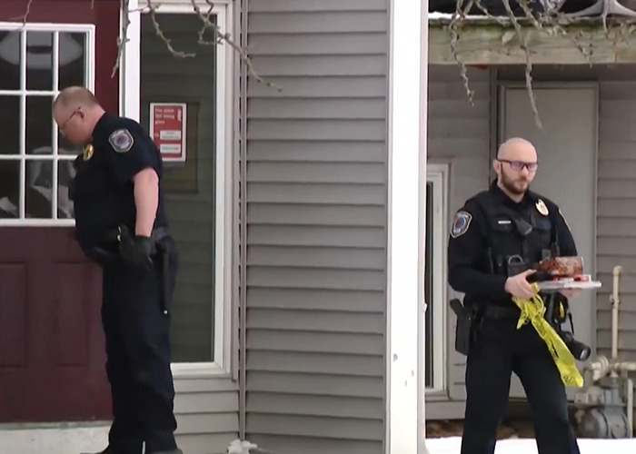 Two police officers outside a house with crime scene tape, linked to a haunting 911 call investigation.