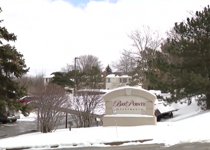 Snow-covered Bay Pointe Apartments entrance sign with trees and buildings in the background on a cloudy winter day.