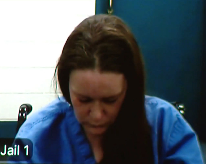 Woman in blue prison uniform with head bowed during a video call, related to haunting 911 call and mom's confession.