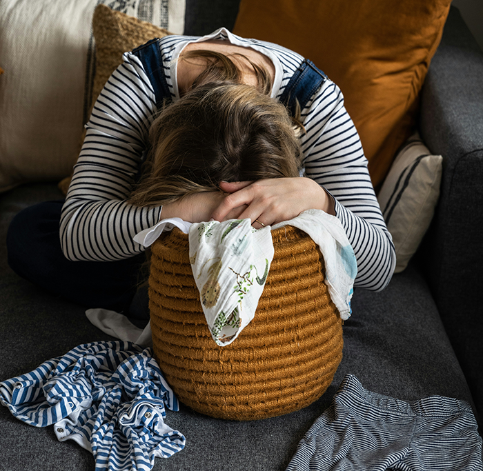 Young woman with head down on woven basket near scattered clothes illustrating clean f***k mom daughter clothes drawers stress.