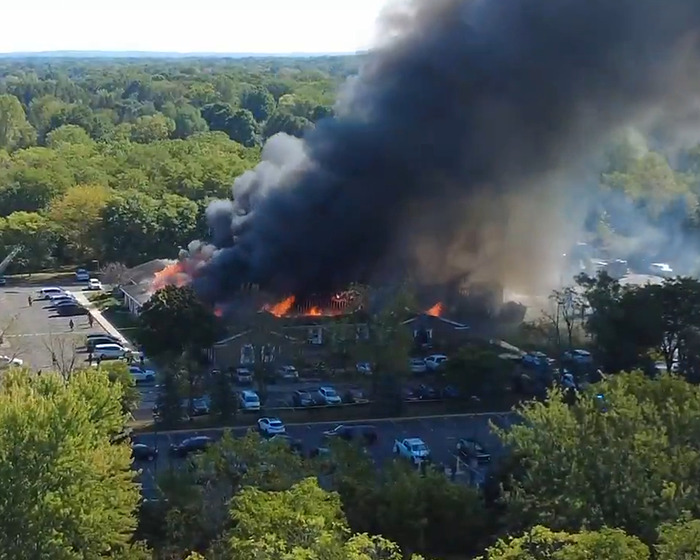 Large fire and thick smoke engulf a Michigan church attacked by a man while many cars are parked nearby in the lot.