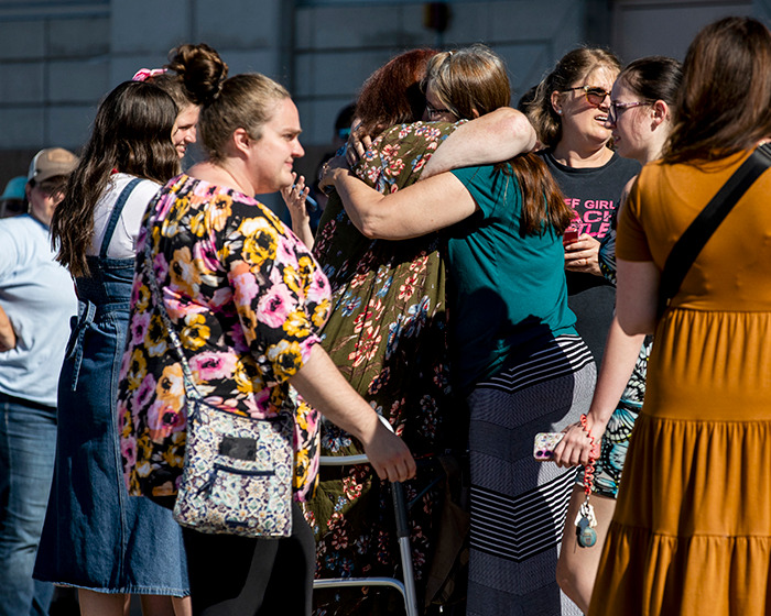 Group of people hugging and talking outside a building after a Michigan church attack involving Mormons raising funds.