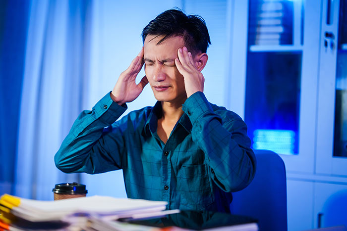 Man in blue shirt holding temples in pain, illustrating self-diagnosed health concerns needing doctor correction.