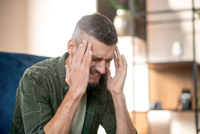 Man in green shirt holding his head in pain, illustrating self-diagnosed health mistakes and doctor corrections.
