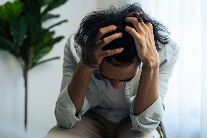 Young man stressed and frustrated holding his head indoors, illustrating self-diagnosed health concerns and medical misunderstandings.