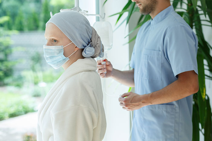 Patient wearing headscarf and mask receiving IV treatment as doctor monitors health during medical diagnosis session.