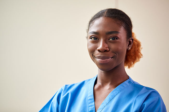 Confident female healthcare professional in blue scrubs smiling, representing doctors correcting self-diagnosis errors.
