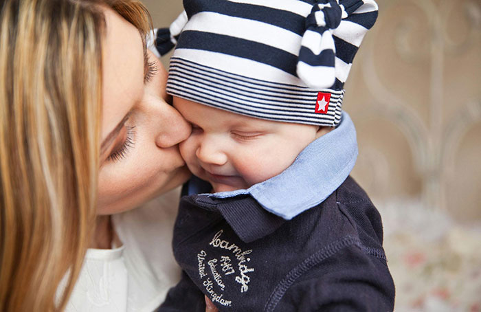 Woman kisses her own baby gently while holding him close, showing affection and love in a tender moment. Woman kisses her own baby gently while holding him close, showing affection and love in a tender moment.
