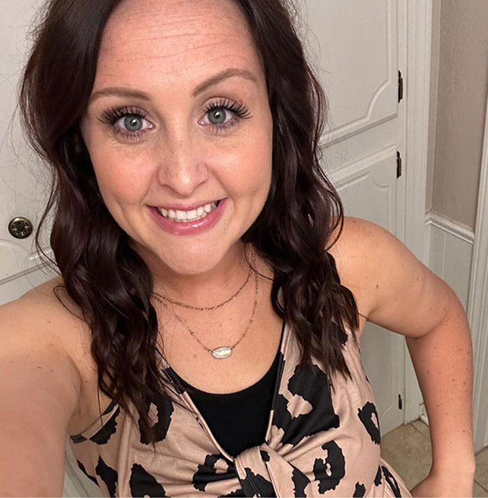 Smiling young woman with dark hair wearing a patterned top, representing a mom affected by a restaurant's drink mistake.