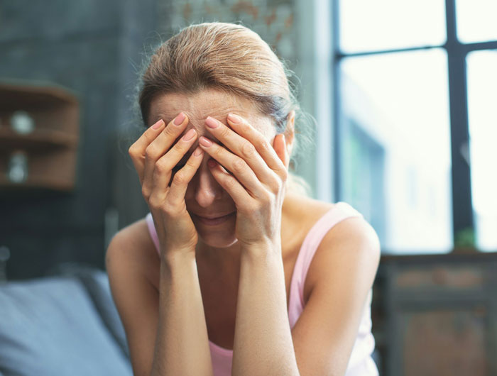 Woman covering her face with hands, appearing stressed, related to twins wanting to include stepmom in group Halloween costume debate.