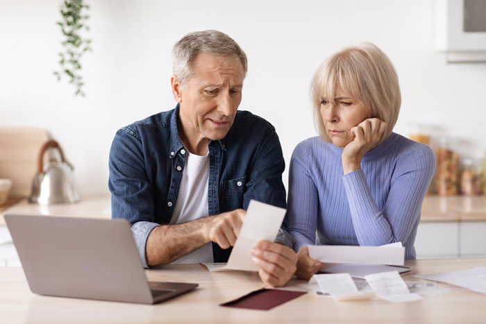 Middle-aged couple reviewing bills at a kitchen table, depicting manipulative parents exploiting financially and emotionally.