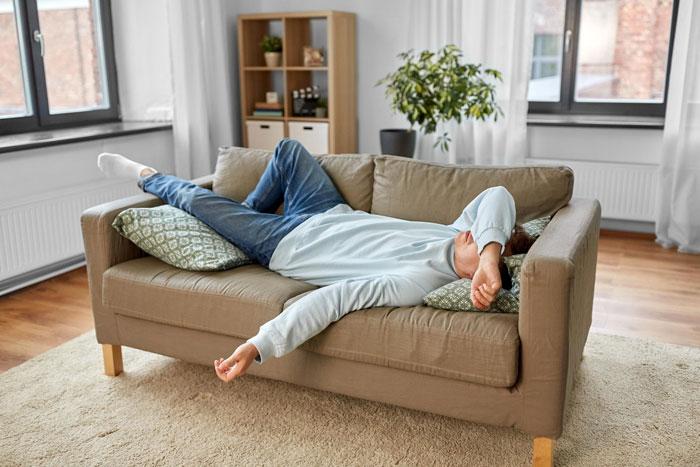 Young man lying on couch looking frustrated and exhausted, illustrating useless bro feeling in a modern living room.