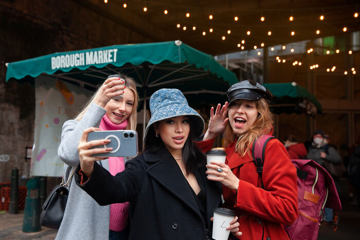 Three women at Borough Market taking a selfie, showcasing multilinguals catching gossip in secret languages they understood.