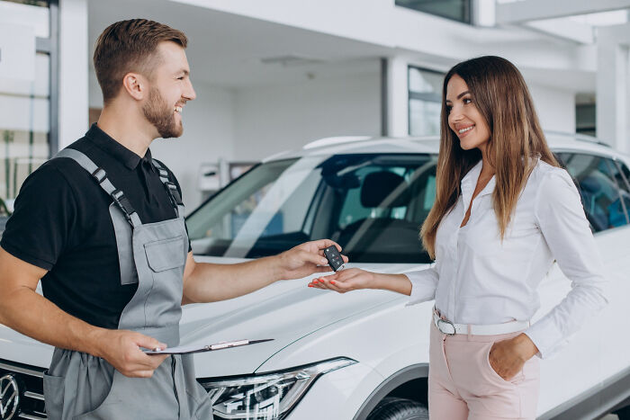 A mechanic handing car keys to a smiling woman, illustrating multilinguals catching folks gossiping in secret languages.