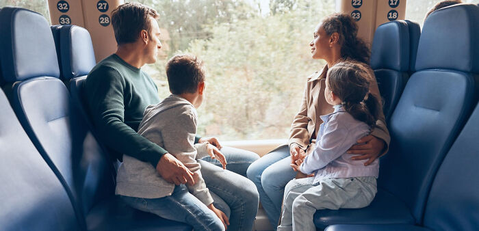A multilingual family sitting together on a train, observing the outside view while engaging in conversation.