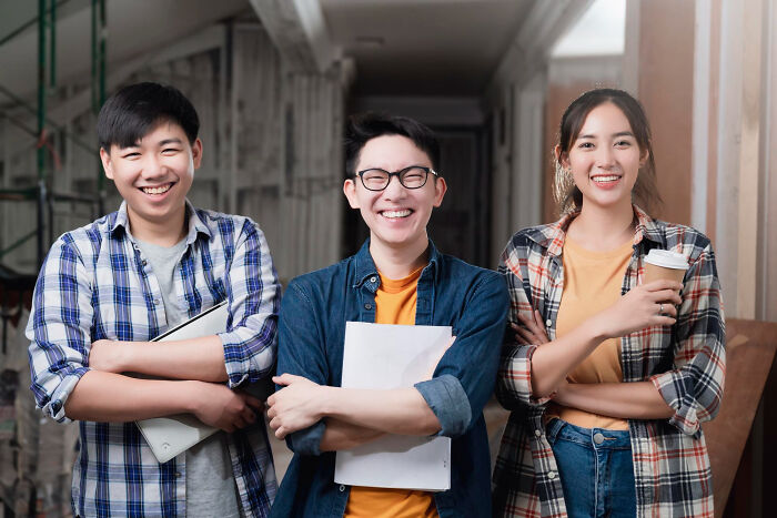 Three multilingual young adults smiling confidently while holding papers and coffee, symbolizing catching gossip in secret languages.