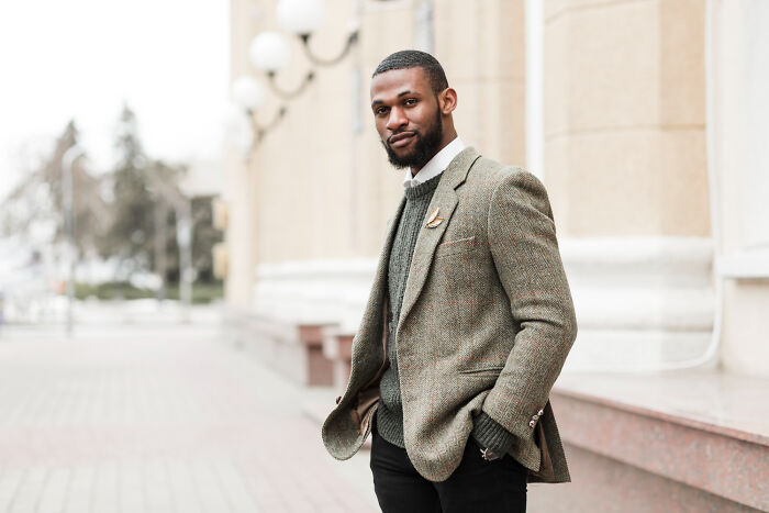 Young multilingual man in a gray blazer standing outdoors, symbolizing catching folks gossiping in secret languages.