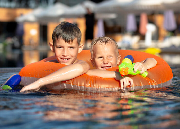 Two multilingual kids laughing and playing in a pool, enjoying catching folks gossiping in secret languages.