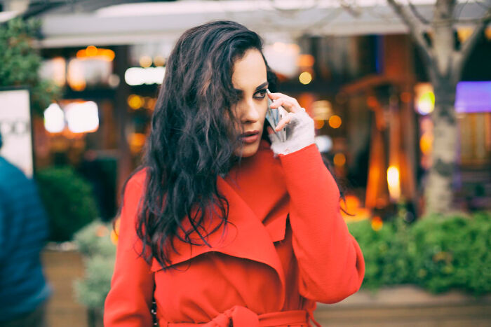 Woman in red coat talking on phone outdoors, illustrating multilinguals catching folks gossiping in secret languages.